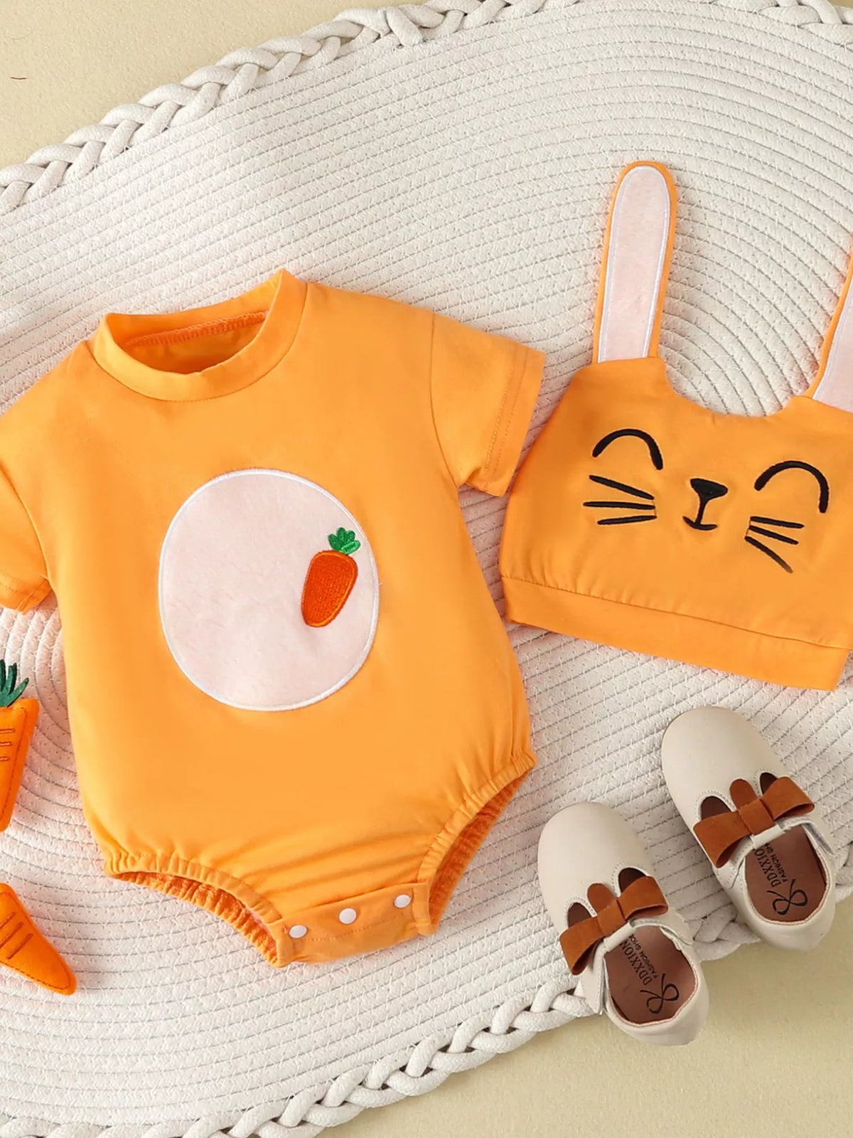 Orange carrot-applique bodysuit with a bunny-ear hat laid flat