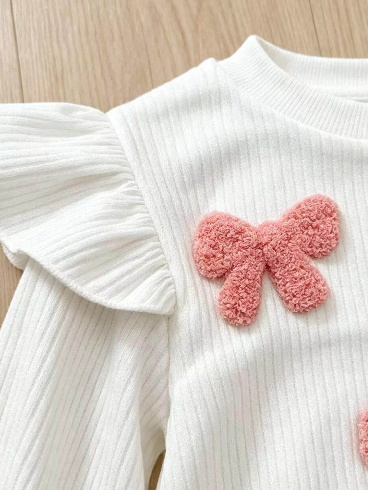 Pink textured bow beside a white shoulder ruffle