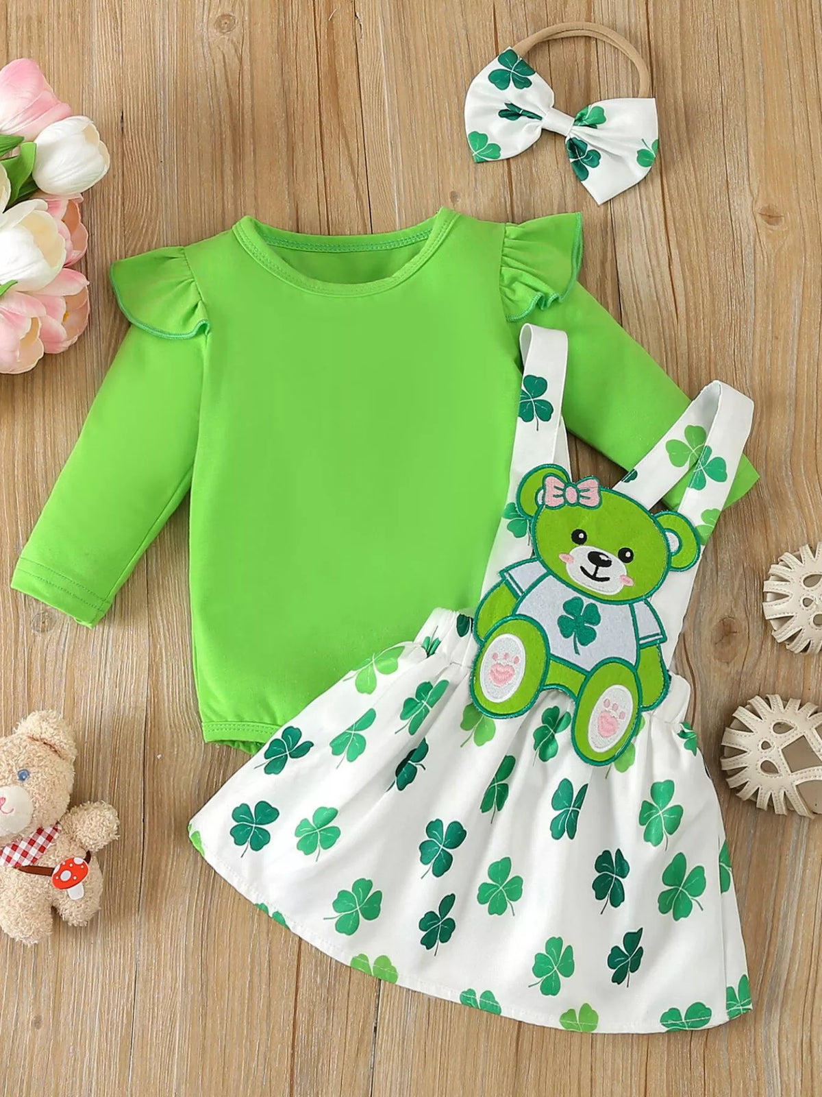 Green ruffle-sleeve bodysuit with a clover-print overall dress and headband laid flat