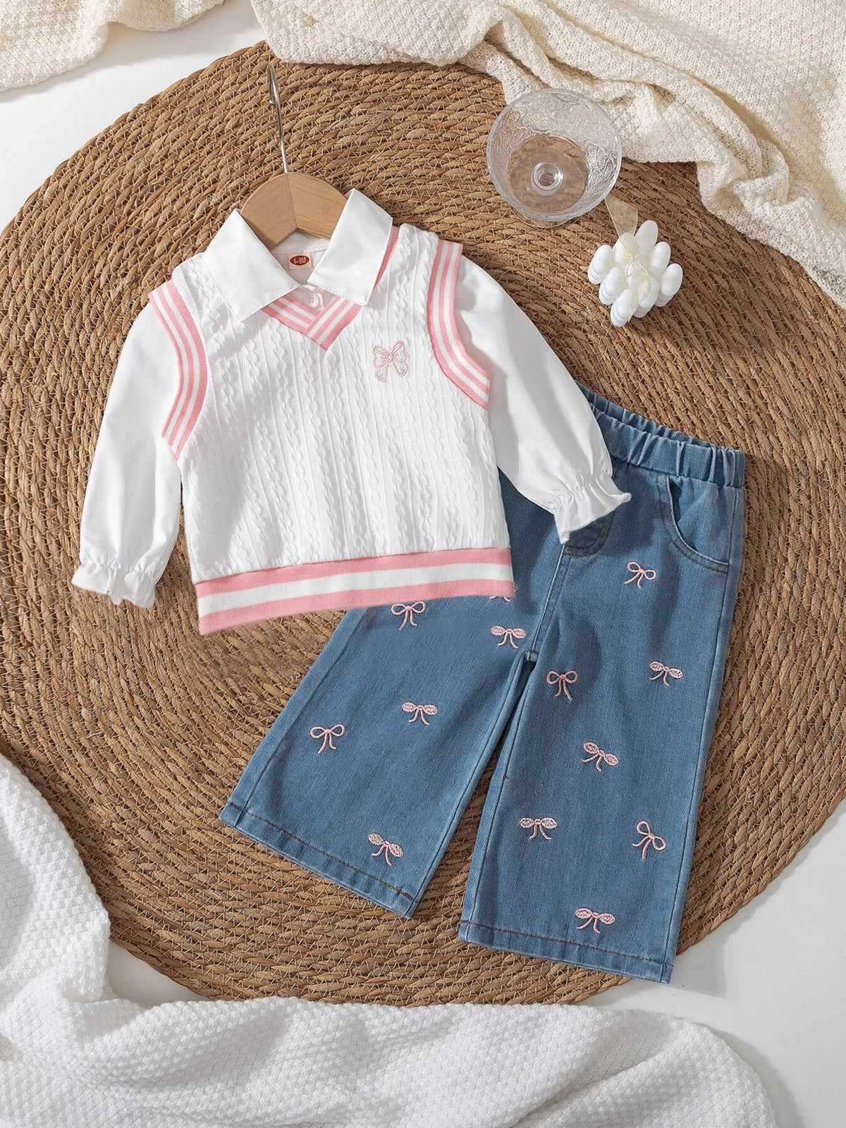 White collared knit-look top with pink trim and bow-detail jeans laid flat