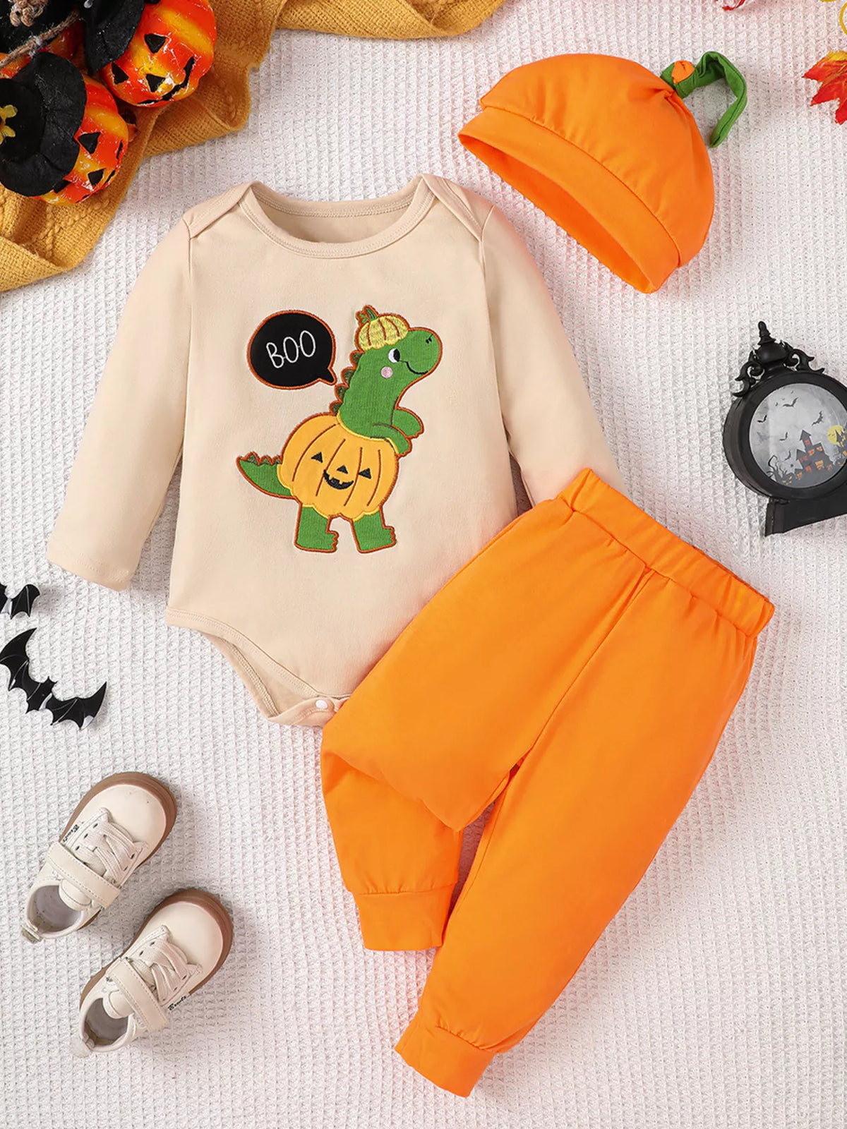 Green dinosaur outfit with orange pants and pumpkin hat laid flat