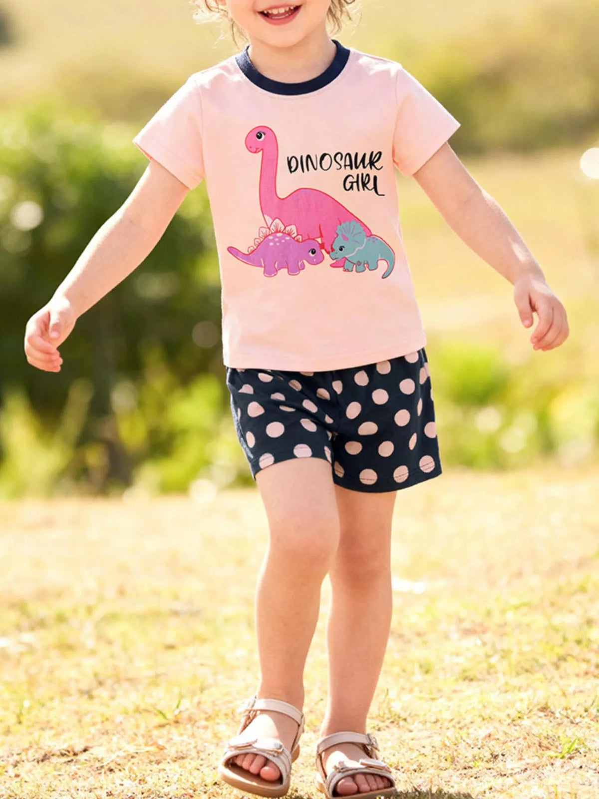 Pink dinosaur tee with navy polka-dot shorts on a child