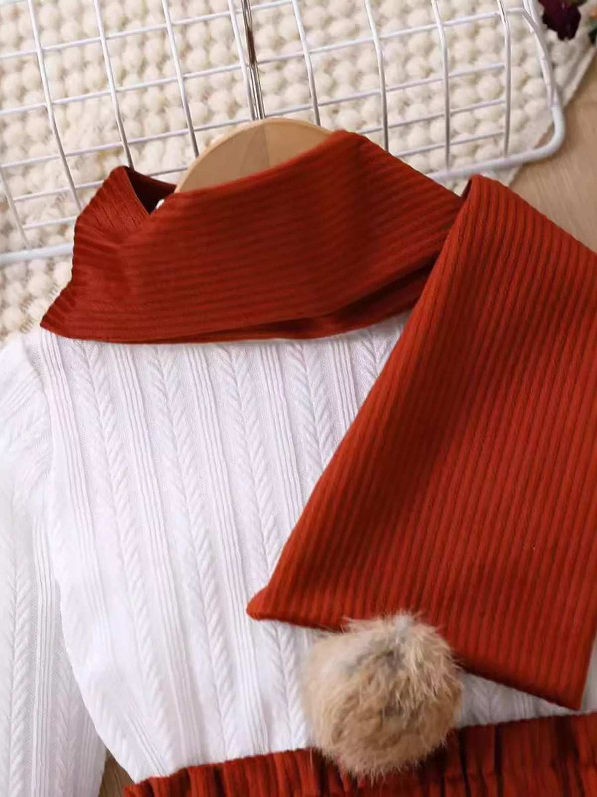 Rust scarf and pom-pom over the white ribbed top