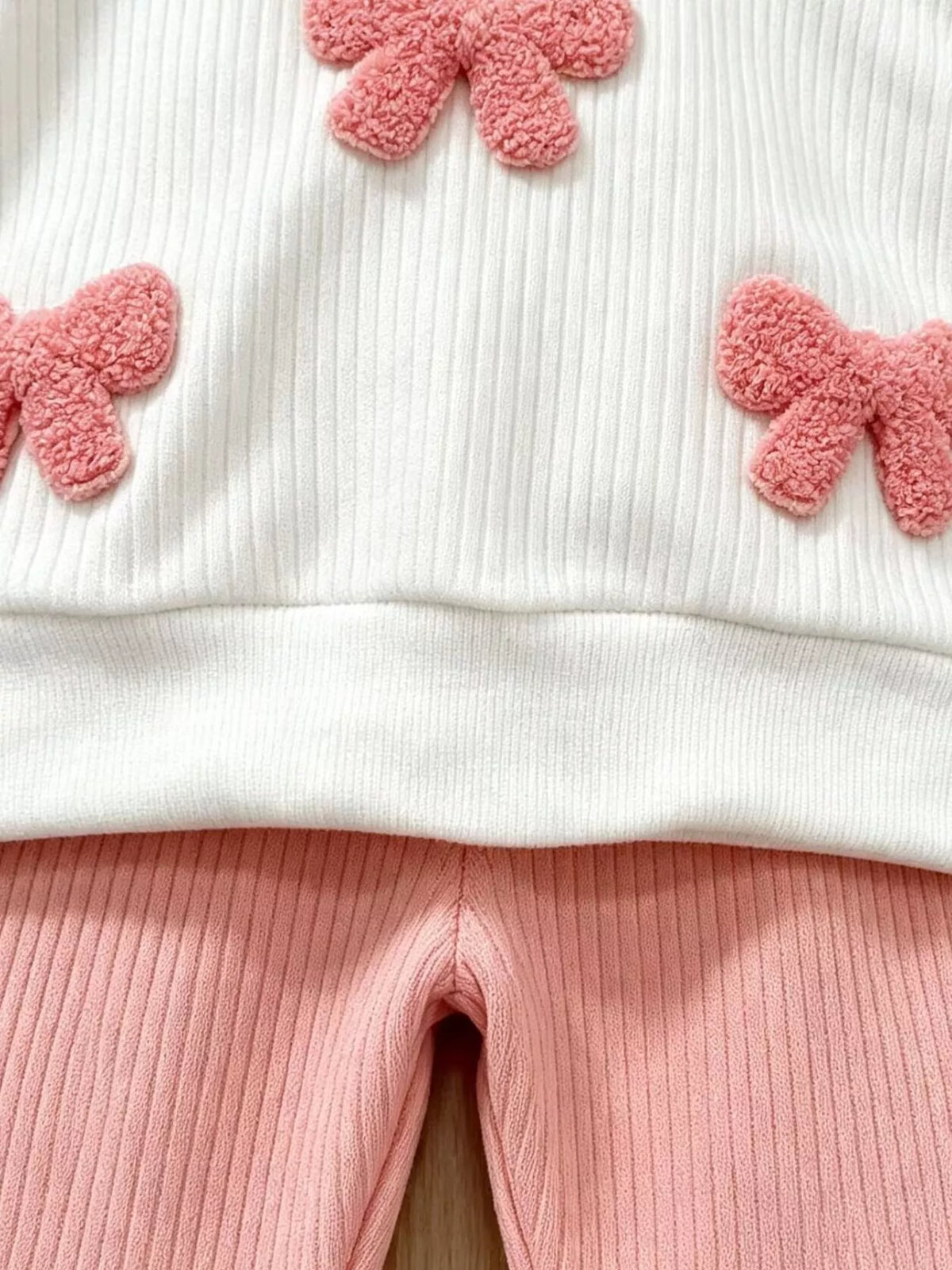 Pink bow appliques above the white ribbed hem