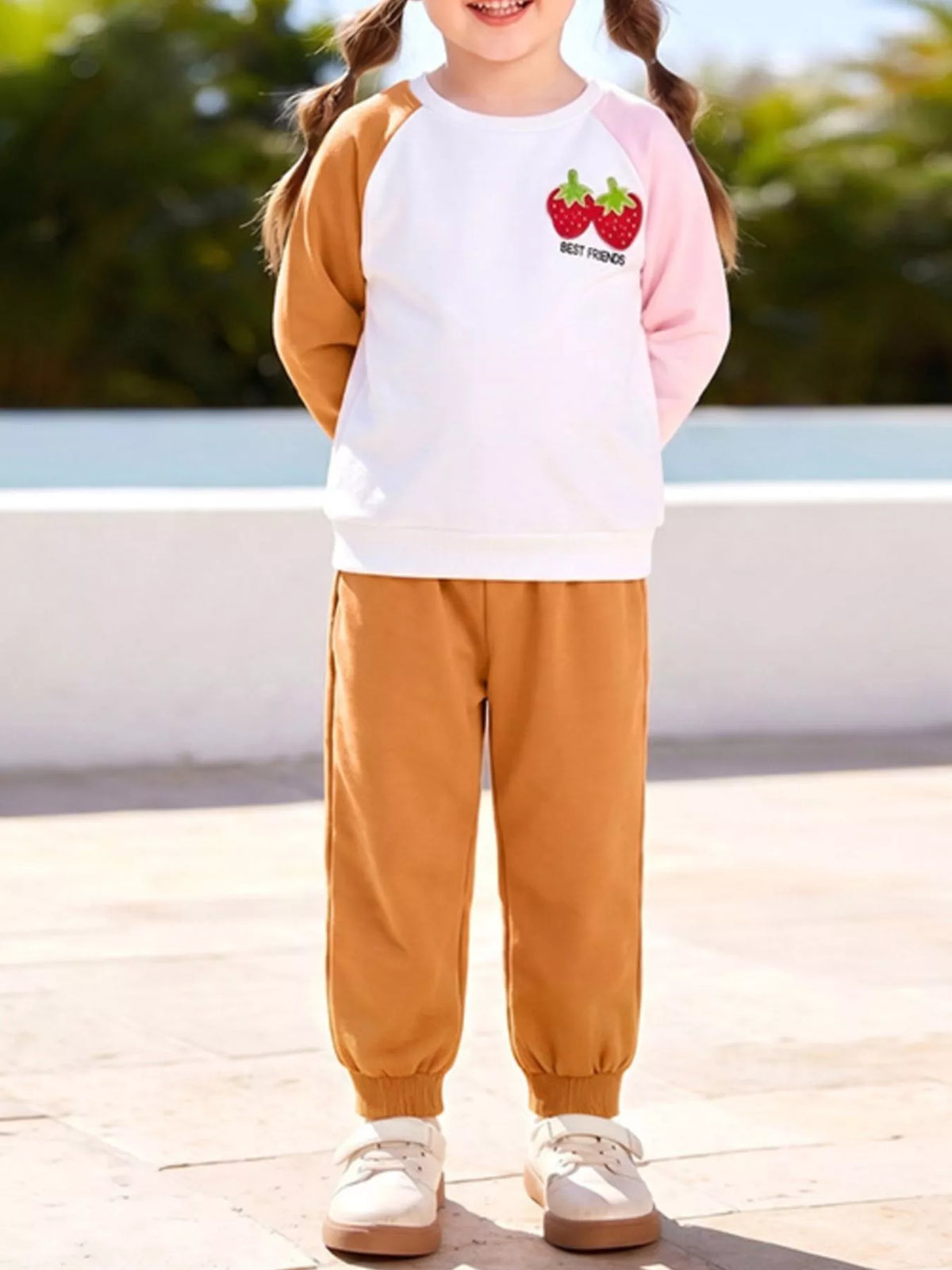 White strawberry sweatshirt with pink and caramel sleeves and caramel pants on a child
