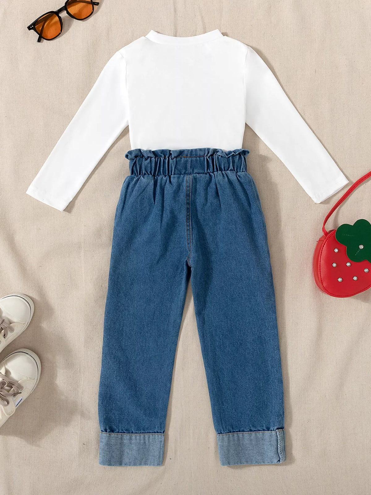 Back of the white top and jeans beside strawberry bag
