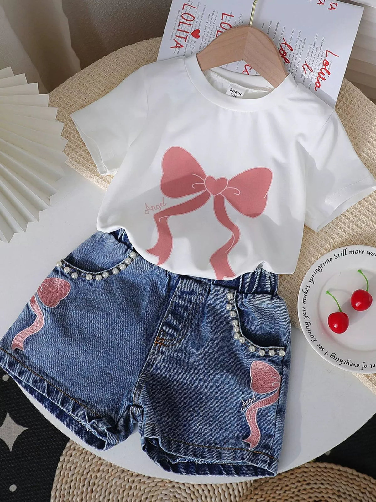 Bow graphic tee and bow embellished denim shorts set — white tee set laid flat