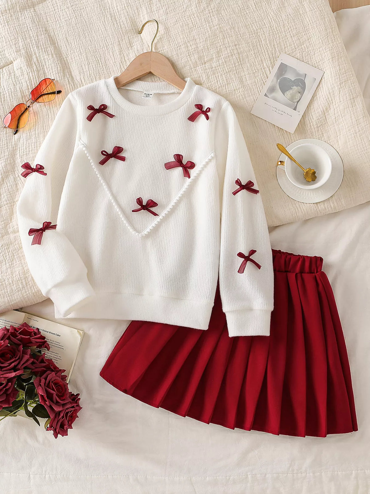 Cream burgundy-bow top with a burgundy pleated skirt laid flat