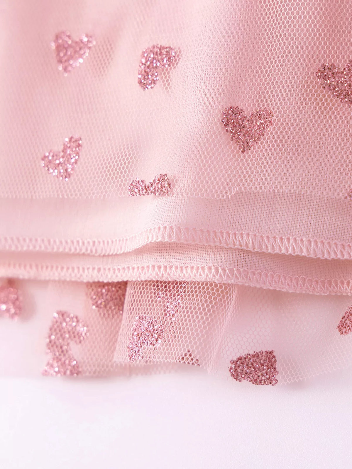 Pink heart motifs on tulle with visible hem stitching