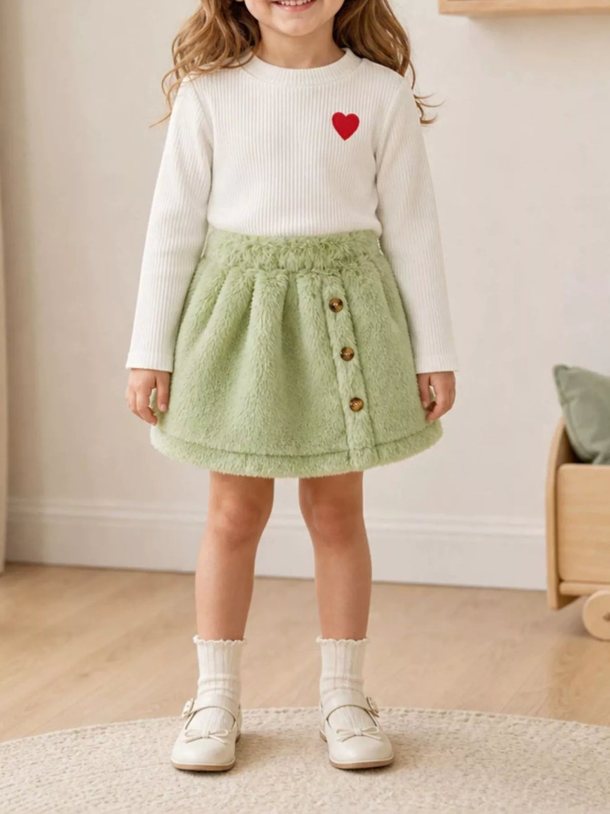 White heart-embroidered top with a green fuzzy skirt on a child