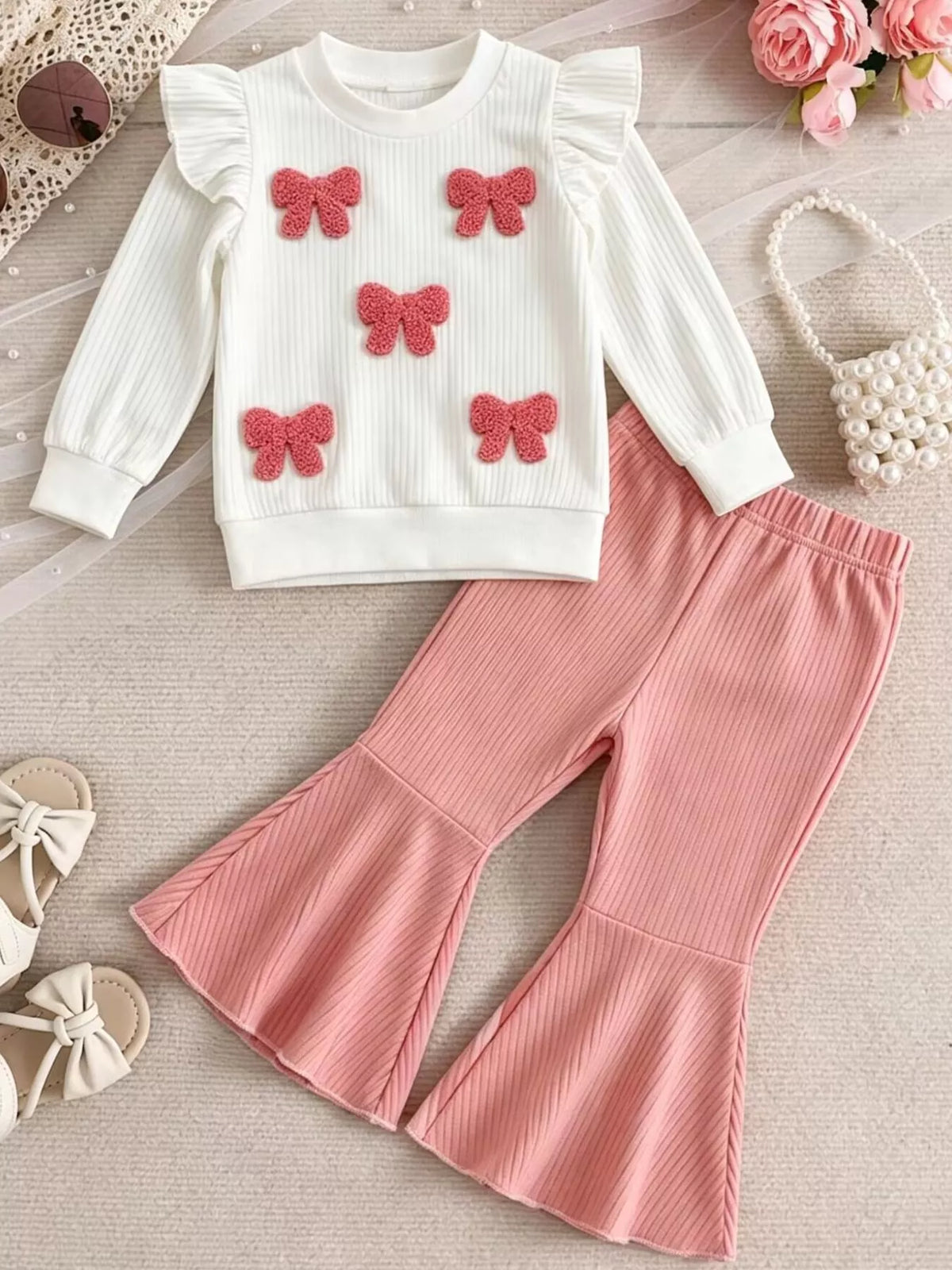 White textured-bow ruffle top with pink flared pants laid flat