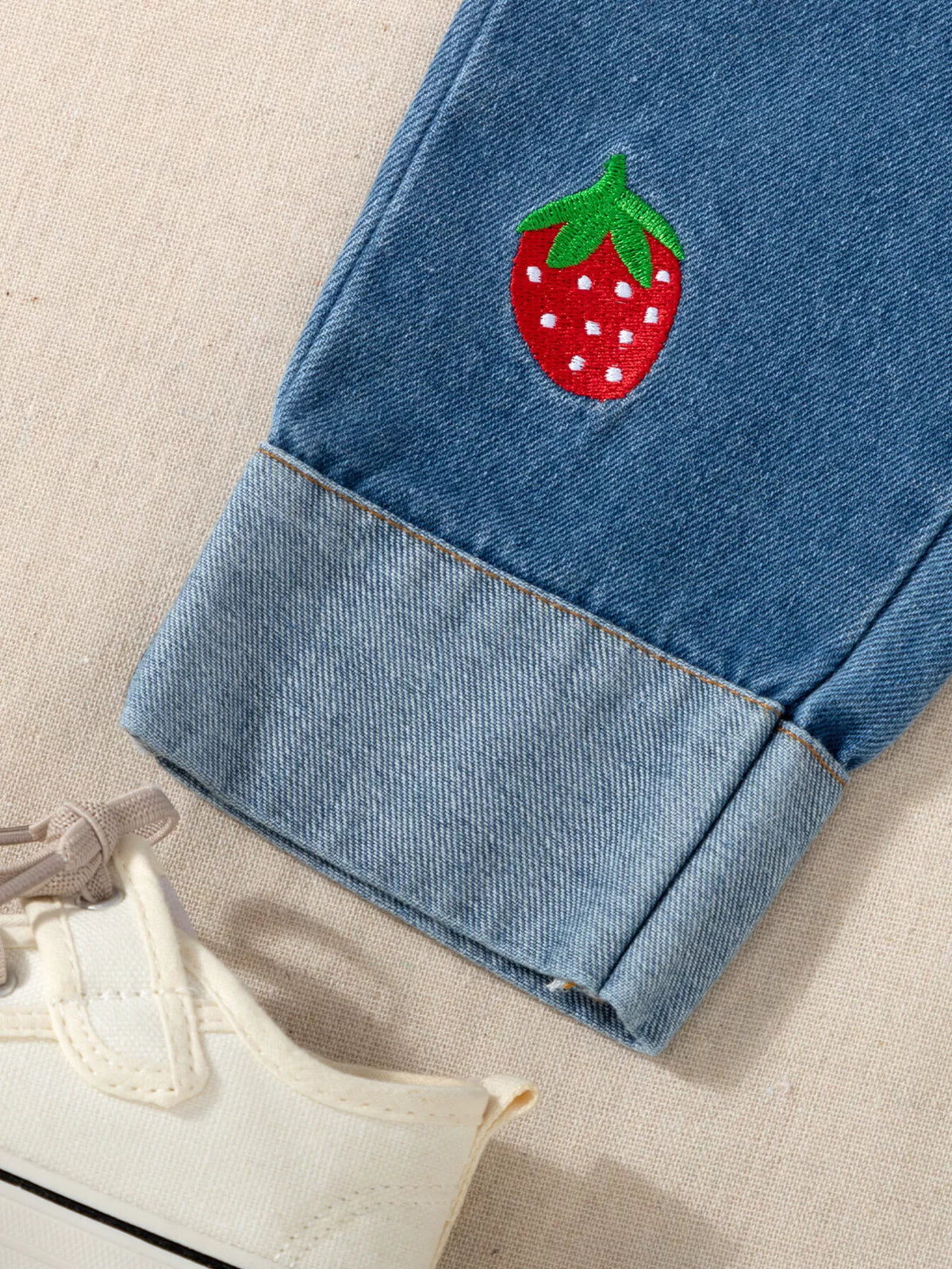 Strawberry applique above the turned-up denim cuff